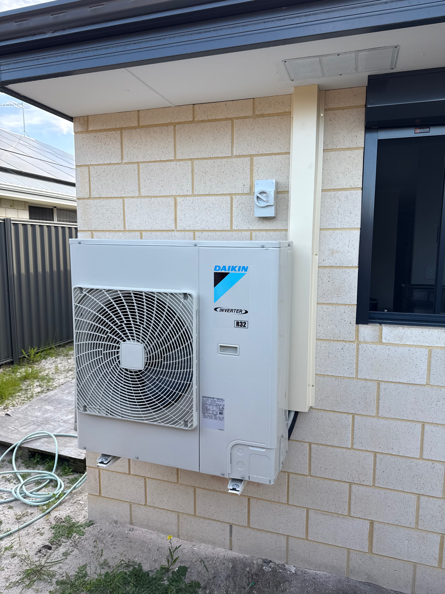 Daikin inverter split system outdoor unit installed on a brick wall with isolator switch and conduit